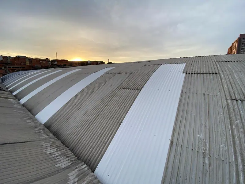 Um telhado em arco depois da obra, com faixas de telhas novas, brancas, ao pôr do sol
