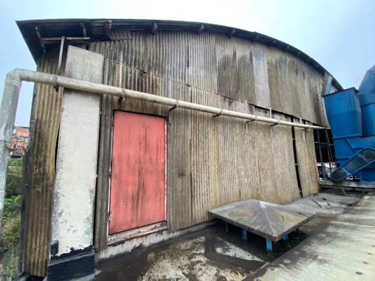 A fachada de um galpão antes da obra, com as telhas antigas escurecidas e uma porta vermelha